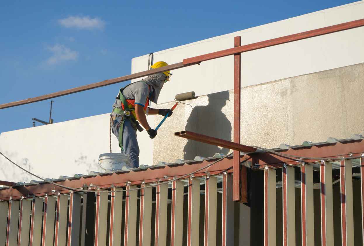 builder worker painting façade of high-rise building with roller